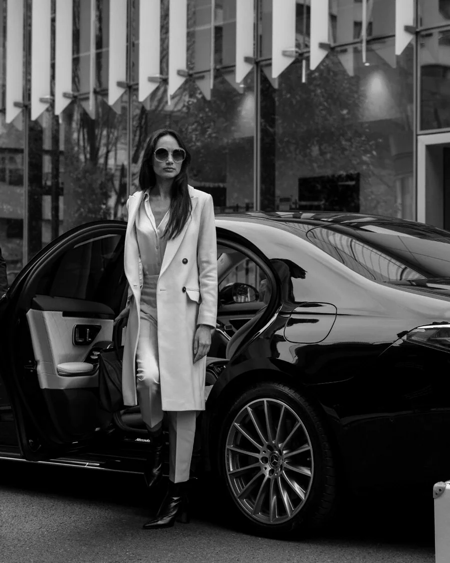 Executive passenger stepping from a black luxury sedan with a professional chauffeur