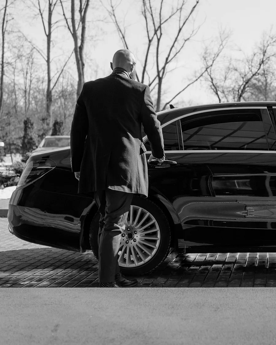 Professional chauffeur opening the door of a black executive sedan